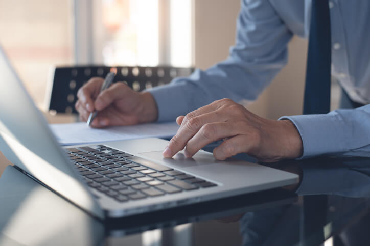 A focused male accounting clerk writing a financial report on a laptop computer after accounting training